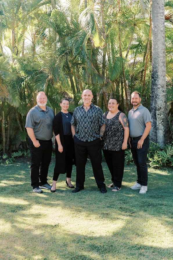 Group photo of the Impact Actual team standing outdoors in front of lush tropical greenery. From left to right: Patrick Mullins, Melissa Dockum, Rob DuBois, Tricia Drago, and Jason Rowinski. All are smiling and dressed in business casual attire.